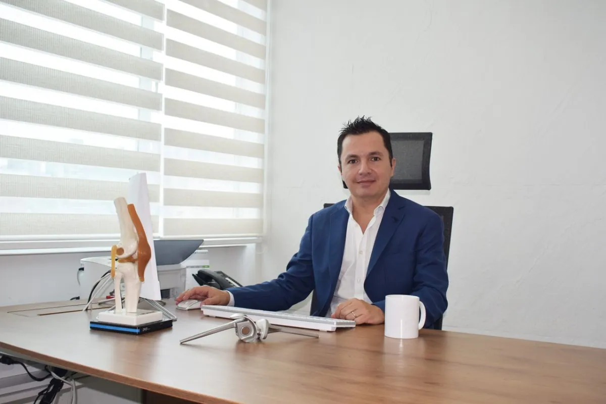 El Dr. Alejandro Jaramillo en su consultorio, junto a un modelo anatómico de rodilla